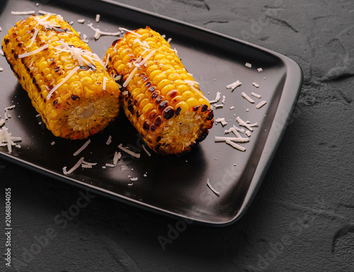 Fotografía Grilled corn cobs with grated cheese on black plate