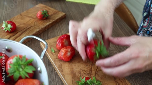 Slicing fresh organic strawberries on olive wood cutting board in kitchen. Close up shot of amateur cook hands preparing sweet summer berries reflecting mindful lifestyle and conscious consumerism