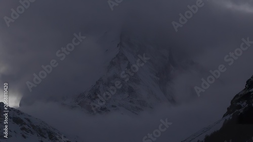 Bild auf Leinwand Snow covered mountain peak shrouded in clouds in a cold landscape