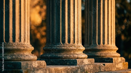 Classical fluted stone columns in golden hour sunlight at sunset. Antique marble pillars on weathered base for law, history, and architectural projects.