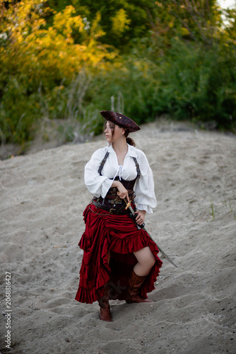 Foto Full-length portrait of a young woman dressed in a pirate costume posing with a saber in her hands while standing against the backdrop of the shore