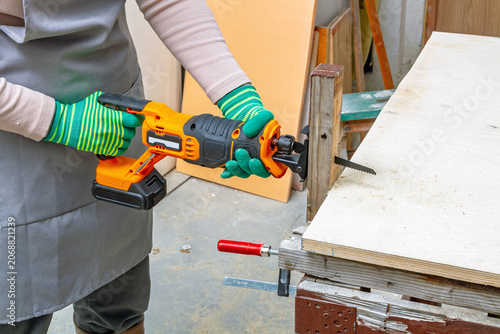 Bild auf Leinwand Woman carpenter using electric reciprocating saw to cut wooden block