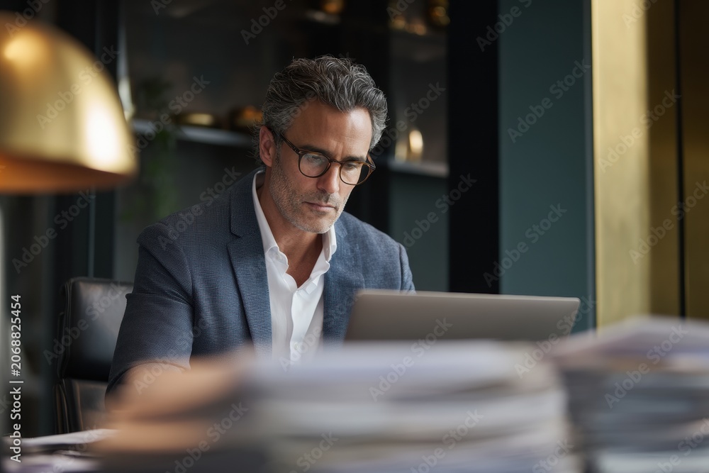 Obraz premium Businessman with glasses working on laptop in modern office. Focused manager typing on computer. Professional career and corporate workplace concept. Serious executive analyzing data.