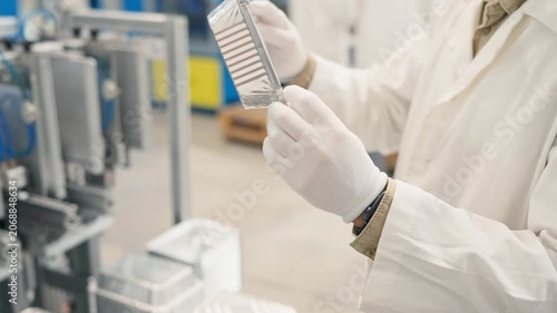 Worker hands wearing white gloves holding and rotating aluminum food container. Inspecting product quality in industrial plant. Clean factory environment focused on manufacturing precision.