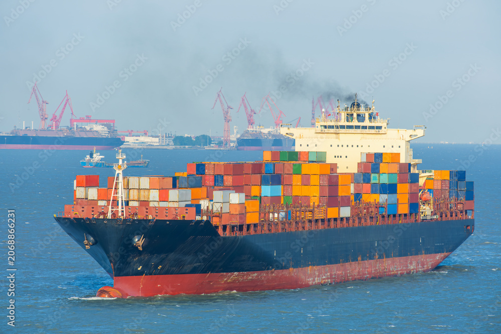 Fototapeta premium Container ship loaded with multicolored freight containers sailing near Shanghai port facilities. International maritime trade, global logistics, cargo transportation, import export operations