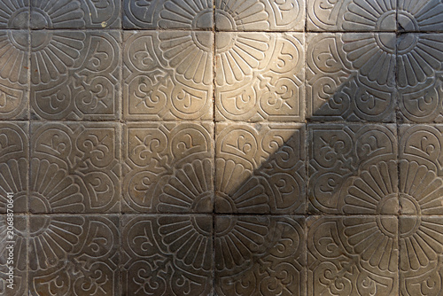 Vintage concrete floor tile pavement featuring traditional embossed floral patterns under high contrast bright natural sunlight and sharp shadow details, perfect for rustic abstract texture background