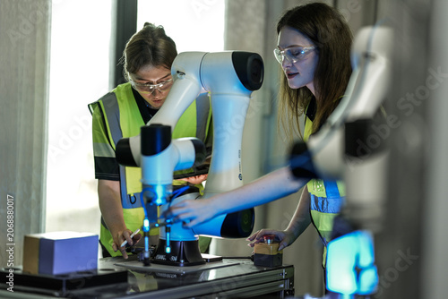 Obraz na plátně Young female scientists collaborating on robotic arm calibration and AI testing in a bright, modern automation laboratory
