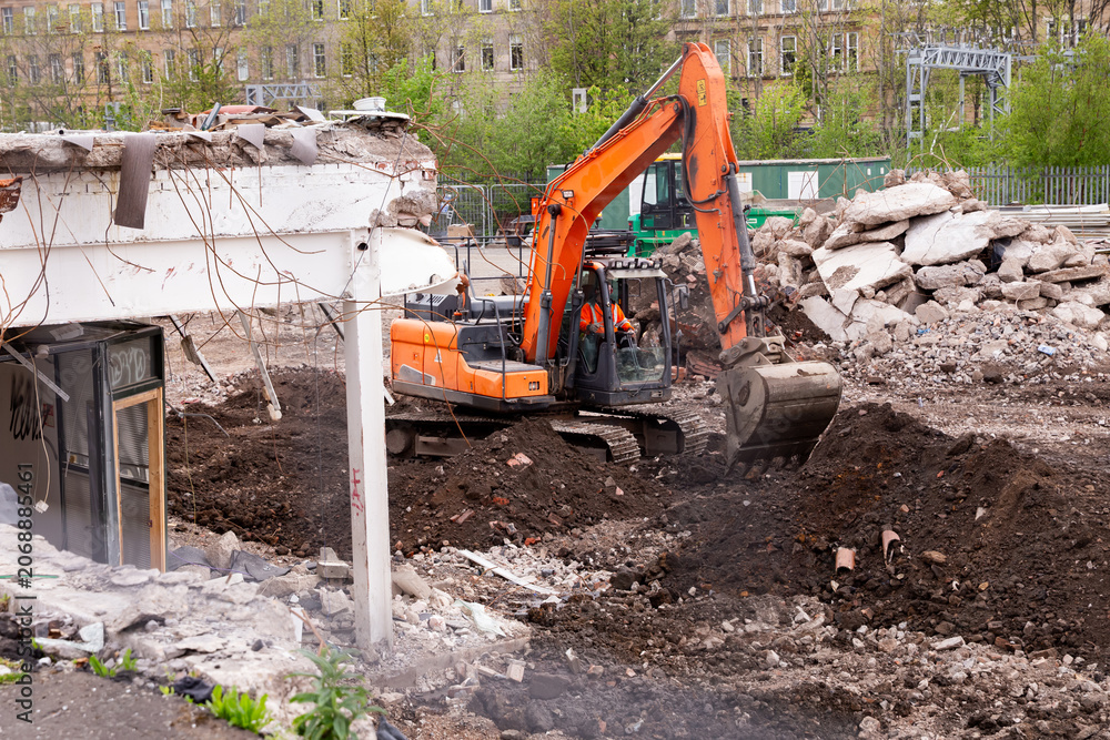 Fototapeta premium Orange excavator working on demolition site clearing concrete debris and rubble.
