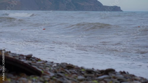 Pebble beach shoreline with breaking waves and orange buoys at near-end of stormy sequence