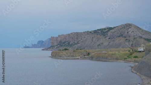 Rocky coastal cliffs revealed through calm sea panorama near sequence end, shoreline curving from
