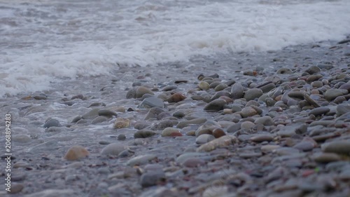 Pebble beach shoreline with waves washing over rounded stones at near-end sequence
