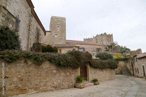 Scenic view of a historic cobblestone street and stone walls leading to the medieval Church of Santa Maria la Mayor and the ancient castle fortifications in Trujillo, Caceres, Spain.