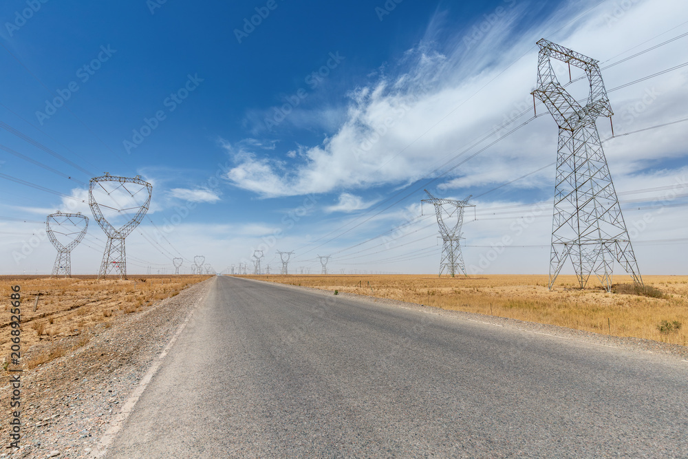 Obraz premium Desert Highway Flanked by High-Voltage Transmission Towers Under Expansive Blue Sky