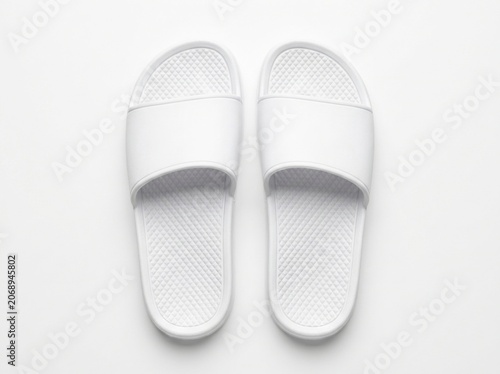 White slide sandals resting on a clean white surface in a minimalist top-down view for spa and hotel amenity marketing