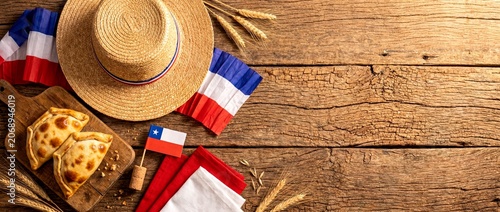 Chilean fiestas patrias celebration with traditional empanadas, straw hat, chilean flag, and wheat on a wooden table