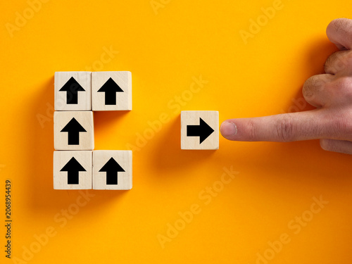 A finger forces a wooden block back into alignment with the group, symbolizing social pressure, corporate rules, and suppressing deviation.