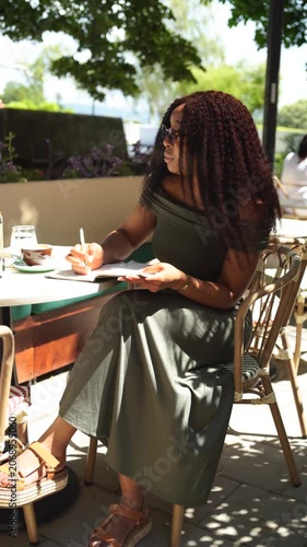 Young woman in a cafe outdoors writing in a notebook on a sunny day