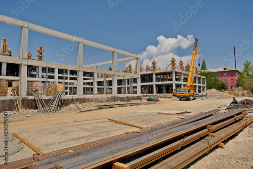 Fotografie Construction site with mobile crane, metal steel rebars on foreground and monolithic concrete framework of a large commercial building project