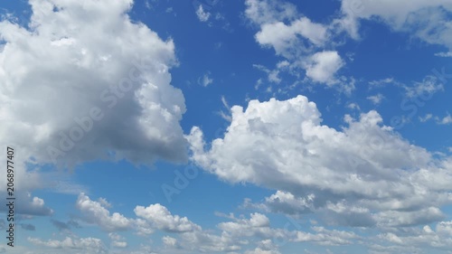 Time lapse video of fluffy white cumulus clouds drifting through a bright blue sky background. Beautiful nature scenery with dynamic cloud movement and sunny weather atmosphere