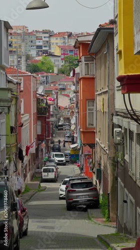 A vertical perspective of a narrow urban street lined with vibrant multicolored houses and parked cars in the historic Balat district of Istanbul under daylight