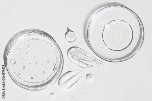 Two petri dishes with liquid bubbles gel smears and drops on light background top view
