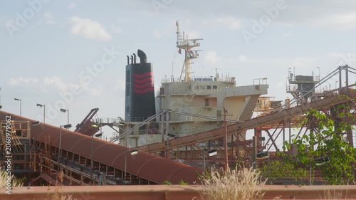 Static view of Port of Weipa in remote Cape York, Australia, with a large bulk ore carrier docked for loading. Vehicle passes by in foreground. Mining export, regional infrastructure. Clip 2