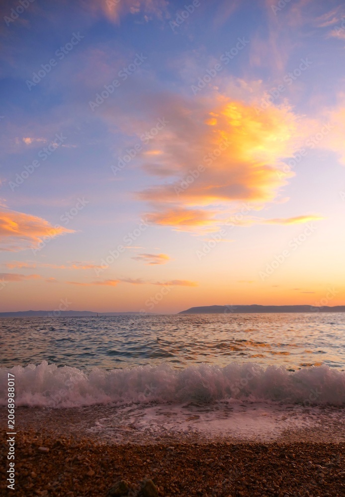 Fototapeta premium Waves on the wind with foam on the sea horizon with colorful clouds in sunset summer sunset background