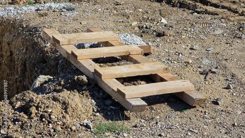 Bild auf Leinwand Homemade wooden ladder lying over trench on dirt construction site