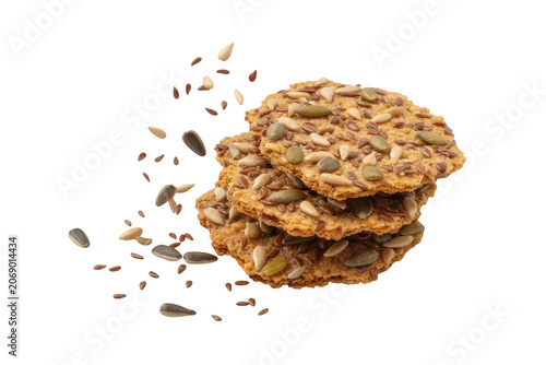 Stack of three round multigrain crackers topped with seeds, with sunflower and flax seeds falling through the air on black background