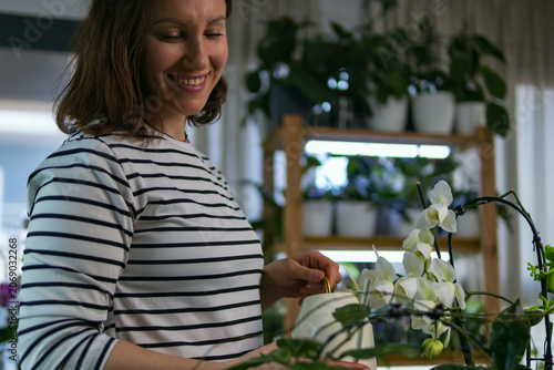 Quadro su tela Young woman smiling, caring for her lush indoor garden, watering a potted white