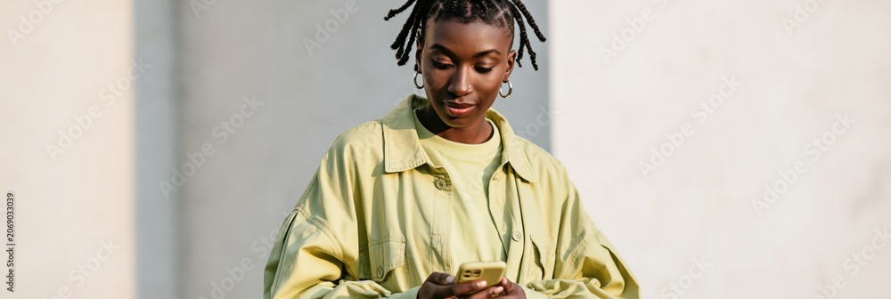 Obraz premium Woman in oversized lime jacket using smartphone outdoor full body portrait for lifestyle banner and social media design and advertising