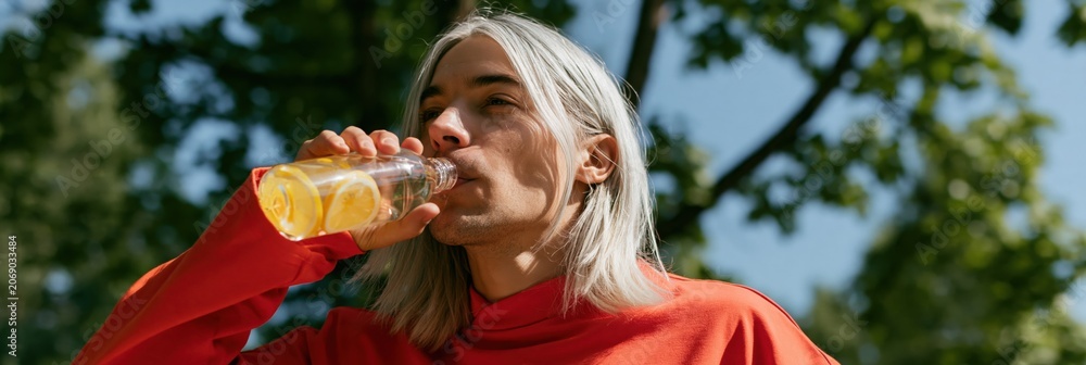 Fototapeta premium Person with long silver hair drinking lemon water outdoors lifestyle background for summer refreshment banner and wellness campaign