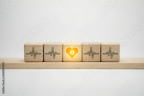Wooden Cubes Showing Ecg Heartbeat Pulse Line with Center Glowing Block Displaying Yellow Heart with Gear Icon for Health Maintenance and Medical Management Concept
