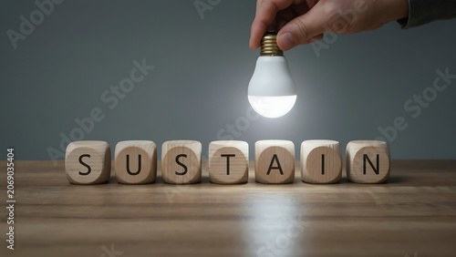 Businessman Hand Placing Glowing LED Light Bulb Above Wooden Cubes Spelling Sustain for ESG Corporate Responsibility and Environmental Conservation Concept