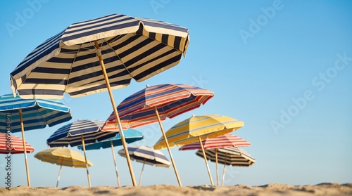 Colorful striped beach umbrellas lined up on sandy shore against blue sky