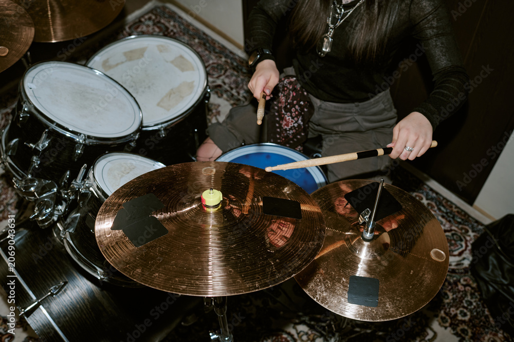 Fototapeta premium Young adult woman playing drum kit during band rehearsal, performing rhythm and music production. Useful for entertainment marketing, music school promotion, overhead shot