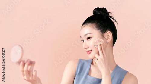 Woman Applying Skincare Routine With Compact Mirror In Soft Pink Background