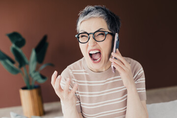 Frustrated middle-aged woman yelling on phone during a heated call at home, expressive emotion and stress captured in candid portrait