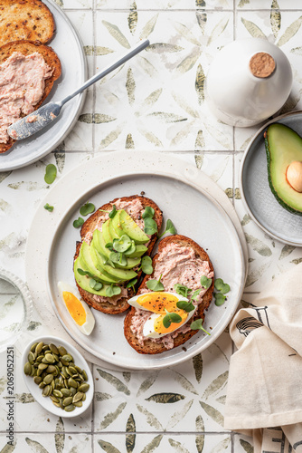 Healthy avocado and egg toasts sprinkled with microgreens and pumpkin seeds on printed tile background top view