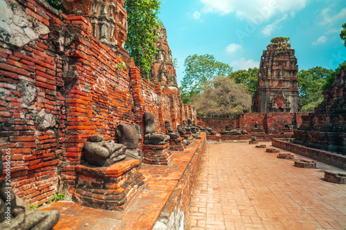 Ancient headless Buddha statues lining the red brick wall at Wat Mahathat in Ayutthaya, Thailand.