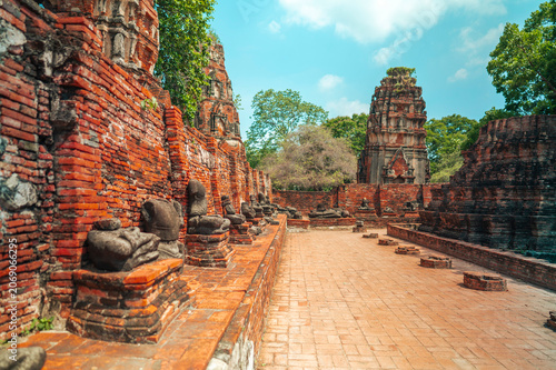 Ancient headless Buddha statues lining the red brick wall at Wat Mahathat in Ayutthaya, Thailand.