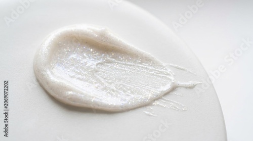 White shimmery cosmetic cream swatch with glitter particles on a neutral surface