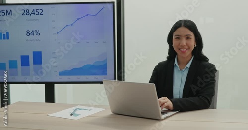Portrait of Asian woman finance expert works on laptop and sits near digital data screen. Japanese businesswoman analyzes stock market in corporate office