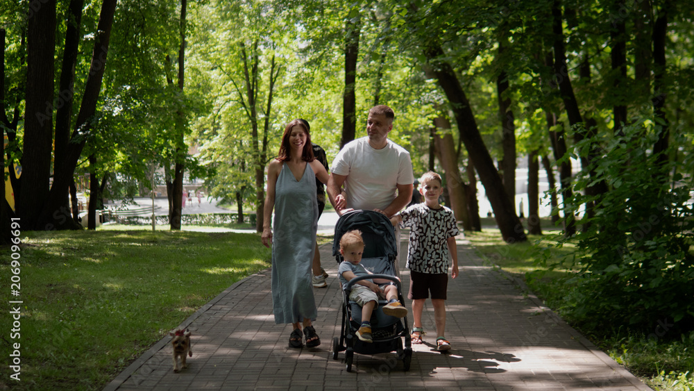 Naklejka premium Young family strolling down shaded tree-lined path in urban park during daytime