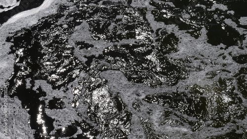 Cuadro en lienzo Dark water covered with irregular slick patches, bright sunlight reflections, an