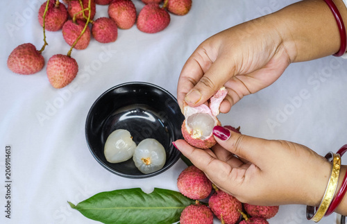 A woman hand Holding a Freshly Peeled Lychee Fruit, Revealing Its Juicy White Flesh and red Outer Shell on keep black bowl. inside with another whole lychee or litchi fruits.