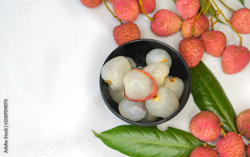 Fresh ripe red Litchi or lychee fruits with green leaves and lichi branch, peeled halves showing white pulp on black bowl, isolated on white background