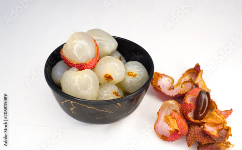 Pile of Peeled red litchi lychee fruits on a black bowl, this side fruits shell and the seeds, isolated on white background,