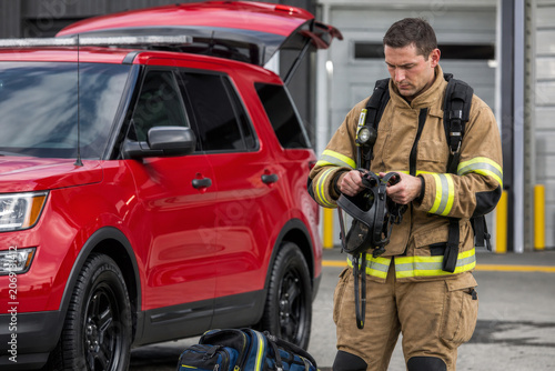 Firefighter prepares his breathing apparatus next to a red emergency vehicle before starting his shift at the station.