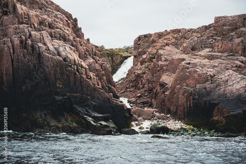 Rugged coastal cliffs with narrow waterfall flowing to rocky shore